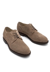 Zapatos de ante marrón con cordones, punta redondeada, suela plana y acentos de cuero contrastantes cerca de los ojetes. Forro interior suave.