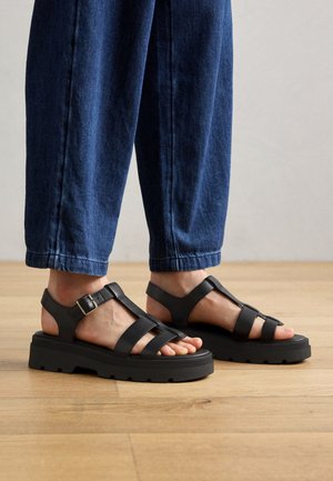 Sandali neri con platform, design a più cinghie, fibbia regolabile e suola in gomma testurizzata. Indossati con pantaloni in denim scuri.