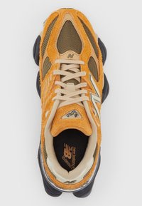 Orange and brown athletic shoe with a textured upper, mesh panels, and black rubber sole. Features cream laces and branding on the tongue.