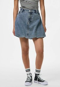 Jupe en denim avec une légère forme en A, couleur bleu clair, ourlet effiloché, et design à cinq poches, associée à des baskets montantes noires et à des chaussettes à rayures.