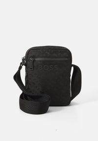 Sac bandoulière noir avec une surface texturée, détail de logo, poche avant zippée et une bandoulière réglable en matériau solide.