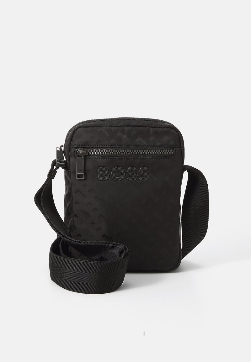 Sac bandoulière noir avec une surface texturée, détail de logo, poche avant zippée et une bandoulière réglable en matériau solide.