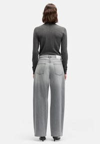 Szerokie spodnie dżinsowe o jasnoszarym kolorze, z wysokim stanem, pięcioma kieszeniami oraz białą metką z tyłu. Materiał wygląda na miękki i lekko sprany.