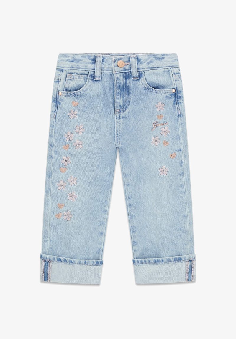 Jean en denim bleu clair avec revers roulés, fleurs roses et cœurs brodés, et un petit logo "Guess" sur la cuisse droite.