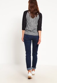 Maglione grigio con maniche in pizzo nero a tre quarti, abbinato a jeans a caviglia blu scuro arrotolati e sneakers bianche.