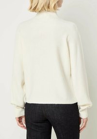 Maglione bianco a maglia con colletto alto a coste, maniche a palloncino e polsini a coste. Il design presenta una vestibilità rilassata e una trama morbida.
