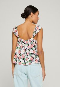 Bluzka w kwiatowy wzór z falbanami na rękawach, z dekoltem w serek. Kolory to różowy, zielony i czarny na jasnym tle.