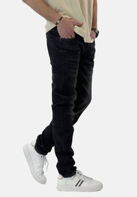 Vaqueros de mezclilla negra con un ajuste slim, que cuentan con cinco bolsillos y costuras sutiles. Combinados con zapatillas blancas acentuadas con rayas rojas y azules.