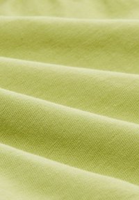 Textúrált szövet lágy világos zöld színben, sima, egyenletes szövésű, finom eséssel, látható redőkkel és gyűrődésekkel.