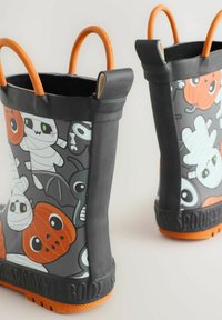 Bottes de pluie en caoutchouc noir avec des graphismes sur le thème d'Halloween, mettant en avant des momies, des citrouilles et des chauves-souris, avec des poignées orange et des semelles texturées.