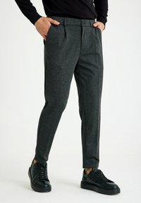 Slim-fit, donkergrauwe broek van belegde stof, voorzien van zijzakken en een gladde tailleband, gedragen met zwarte sneakers.