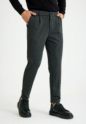Slim-Fit, dunkelgraue Hose aus strukturiertem Stoff, mit Eingrifftaschen und einem glatten Bund, kombiniert mit schwarzen Sneakers.