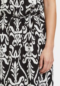Schwarz-weißes Kleid mit floralem Muster, das über einen Taillengürtel und Falten verfügt. Der Stoff hat eine weiche Textur und ein fließendes Design.