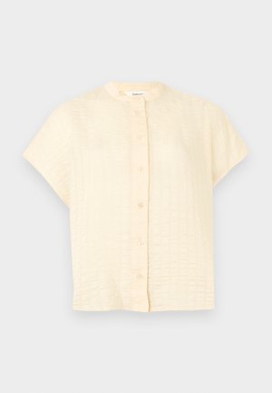 Cream-colored, short-sleeve blouse with a textured checkered pattern and front button closure.