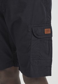 Donkerblauwe cargoshorts gemaakt van duurzaam materiaal. Heeft een zijzak met een bruine leren labelpatch en stiksels.