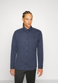 Navy blue button-up shirt with long sleeves, made of textured fabric, featuring a small embroidered logo and contrasting buttons.