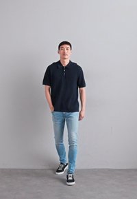 Tengerészeti polo póló rövid ujjal, két gombbal a gallérnál, világoskék slim-fit farmernadrággal és fekete sportcipővel, fehér talppal párosítva.