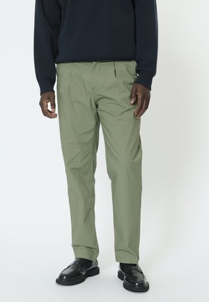 Svetlo olivové nohavice s voľným strihom, vybavené záhybmi, bočnými vreckami a lemami pri členkoch. Kombinované s čiernymi mokasínami a námorníckym sveterom.