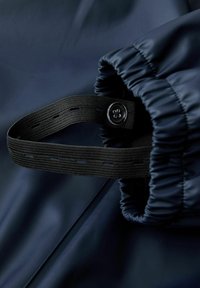 Marinträdes vattenavvisande tyg med ett strukturerat svart elastiskt band och knappdetalj vid manschetten, med samlade kanter för en snug passform.