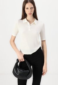 Lys kremfarget polo-skjorte med korte ermer og kneppbar krage, kombinert med tettsittende sorte jeans og en svart hobo-veske.