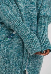 Sweter w kolorze teal, z dzianiny, z ribbnowym wykończeniem rękawów i zamkiem błyskawicznym. Posiada teksturowany wzór w odcieniach niebieskiego i zielonego. Miękki, gruby materiał.