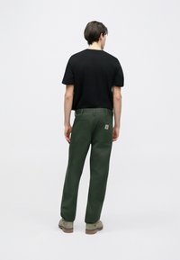 Σκούρο πράσινο παντελόνι εργασίας με ίσια κοπή, δύο πίσω τσέπες και ετικέτα λογότυπου. Συνδυάζεται με μαύρο κοντομάνικο πουκάμισο.