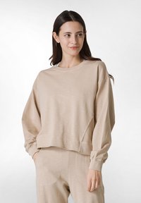 Sudadera corta beige hecha de material suave, con un cuello redondo y mangas largas con puños elásticos, complementada con detalles de costura sencillos.