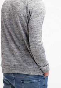Sudadera gris texturizada con un patrón moteado, que cuenta con mangas largas y un dobladillo acanalado, combinada con jeans azules.