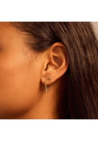 Goldohrringe mit einem V-förmigen Design und einem kleinen, kugelförmigen Akzent, die in einem durchstochenen Ohr auf glatter Haut präsentiert werden.