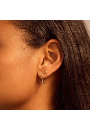 Boucles d'oreilles en or avec un design en forme de V et un petit accent sphérique, portées dans une oreille percée contre une peau lisse.