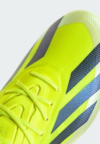 Limegrön fotbollssko med en strukturerad yta, prydd med grå detaljer och lila ränder. Inkluderar platta snören och en stilren, lågprofil design.