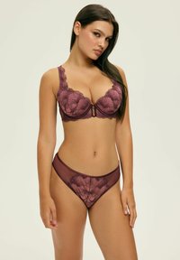 Burgundowa koronkowa biustonosz z kwiatowym wzorem i fiszbinami, w zestawie z pasującymi przezroczystymi majtkami. Posiada falbaniaste krawędzie i centralny element dekoracyjny.