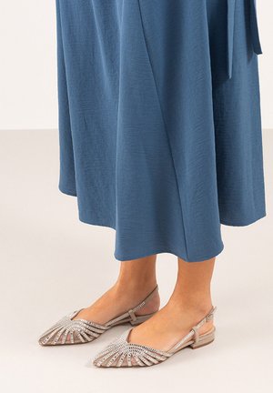 Bailarinas en beige claro con un diseño de recortes geométricos y detalles en plata, combinadas con un vestido de tela azul fluida.