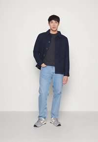 Casaco azul-marinho com botões e colarinho, t-shirt cinzenta, jeans azul claro e ténis cinzentos com detalhes brancos e dourados. Tecido texturado.