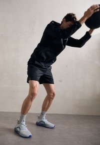 Athletic outfit with a black long-sleeve top and black shorts. Gray-blue sneakers feature a textured sole and blue accents. White socks visible.
