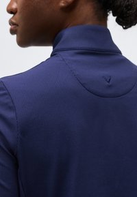 Gros plan d'une personne portant une chemise à col haut côtelée bleu marine, vue de dos et légèrement de côté.