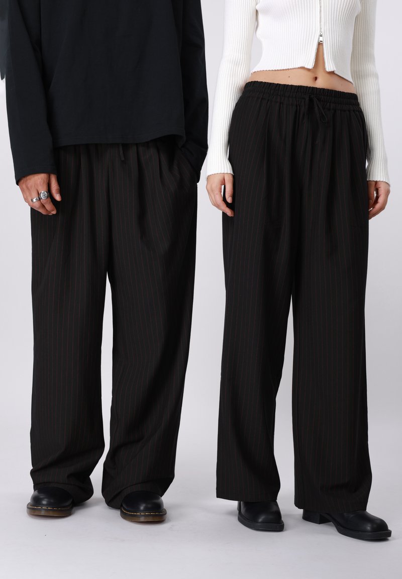 Sorte bukser med striber i afslappet pasform, der har elastik i taljen og snøre-detalje. Glat stof og bred ben-design.