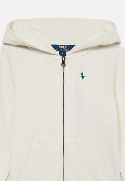Kremna zip-up kapuca iz bombaža s sprednjim žepom, ki ima zeleno vezeno logo na prsih in kapuco s vrvico.