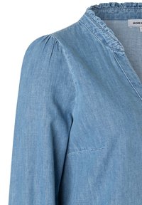 Hellblaues Denim-Hemd mit gerüschtem Kragen, gepufften Ärmeln und subtilen Steppnähten. Der Stoff wirkt weich und strukturiert.