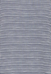 Weißer Stoff mit einem dunkelblauen Gittermuster, das unregelmäßige, handgezeichnete quadratische Formen aufweist.