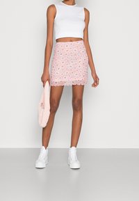Jupe mini rose avec un motif floral de marguerites blanches, ourlet festonné, assortie à un haut sans manches blanc et des baskets montantes blanches. Tient un sac rose.