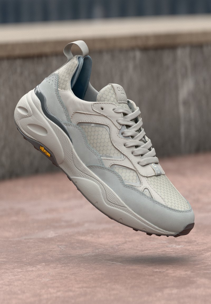 Sneaker, mille kreemja ja heleda halli värviskeemiga, võrgumaterjalist ja seemisnahast, kuuepoolse mustriga, tekstuurse tallaga ja kanna küljes oleva tõmblukuabhiga.