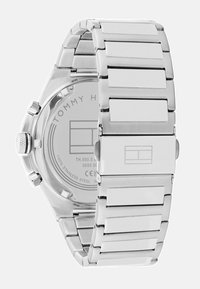 Montre en acier inoxydable argenté avec un bracelet en maillons, présentant un boîtier rond et une surface lisse. L'arrière affiche le nom et le logo de la marque.