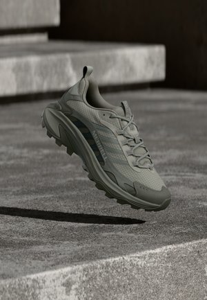 Hellgrauer Trailrunningschuh mit strukturiertem Mesh-Obermaterial, rundlicher Spitze und robustem Profil. Verfügt über Markenzeichen und schnürbares, eng anliegendes System.