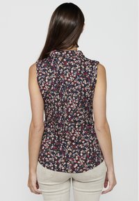 Camicetta senza maniche con motivo floreale su sfondo blu navy scuro, con piccoli fiori rossi, rosa e bianchi, e colletto.