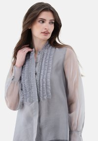 Hellegraue Bluse mit Rüschen-Front-Details und dekorativen Verzierungen. Transparente lange Ärmel und Knopfverschluss am Kragen.