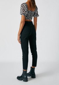 Černé džíny s vysokým pasem a tapered střihem, doplněné o zkrácený top se zebra potiskem v černé a bílé barvě s balónovými rukávy. Hromadné černé kotníkové boty.
