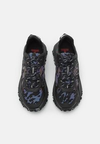 Chaussures de sport noires avec un motif camouflage multicolore, une tige texturée, une semelle en caoutchouc robuste et des lacets réfléchissants.