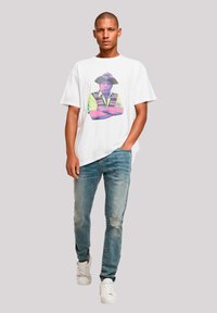 White t-shirt featuring a colorful graphic design of a person wearing a hat. Paired with light blue distressed jeans and white sneakers.