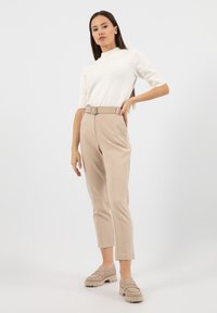 Bílý pletený top s krátkým rukávem spárovaný s béžovými kalhotami s vysokým pasem a tapered střihem se sakem, a béžovými robustními nazouvacími botami.